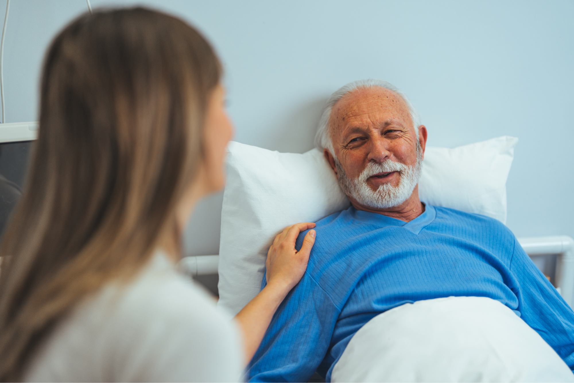 An elderly man laying on a bed, sharing a smile with his senior companion
