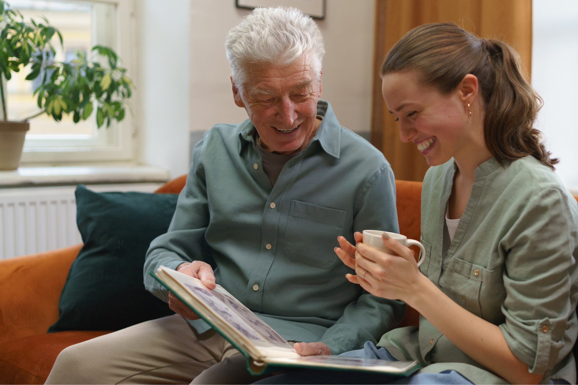 A senior man and his senior companion sitting on a couch together smiling